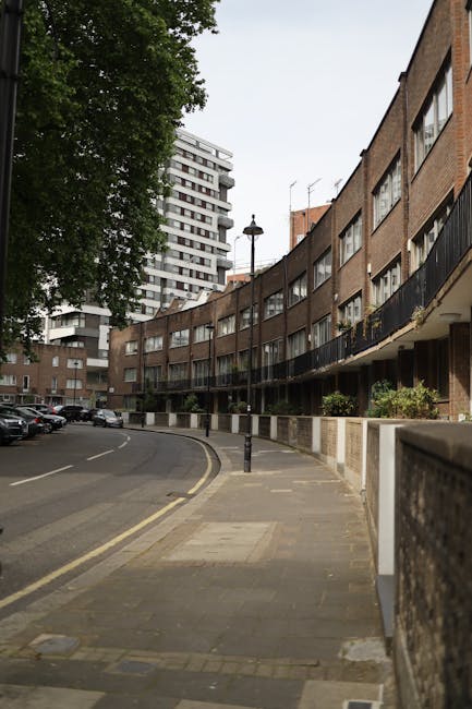 The image depicts the exterior of a red-brick Victorian residential building with multiple large sash windows, some with white frames, and a decorative wrought-iron balcony on the second floor. The en