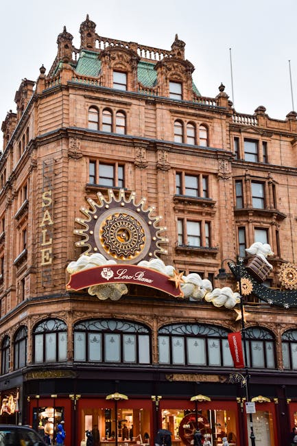 The image shows the exterior of a historic multi-storey building constructed from reddish-brown brick with ornate architectural details and decorative cornices at the top. Large windows are evenly spa