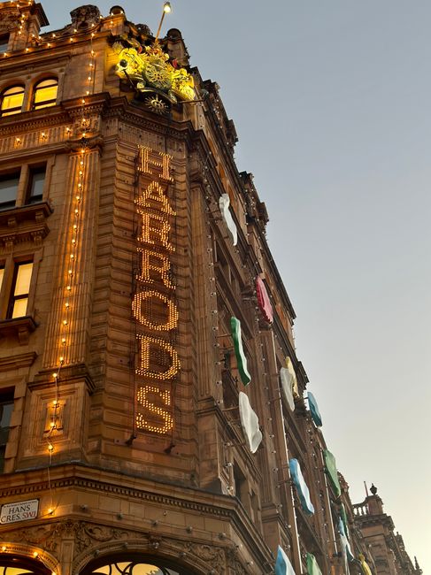 Photograph of the exterior of a historic, ornate building illuminated at dusk, featuring decorative architectural details such as cornices, columns, and intricate stonework. Several colorful laundry c